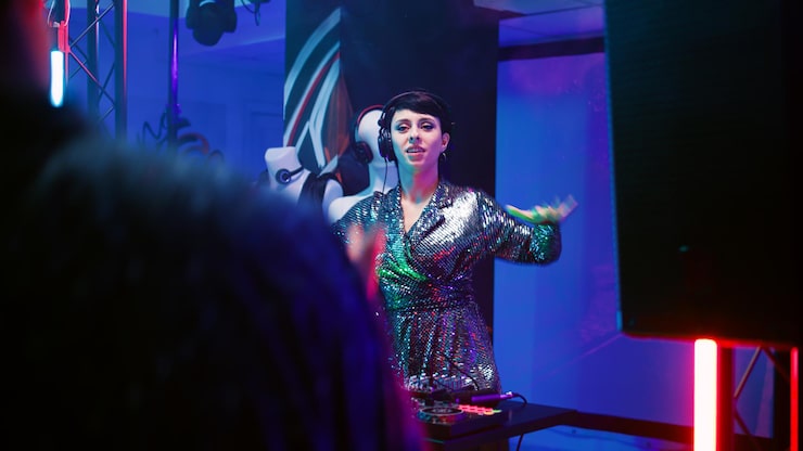 Szeroki kadr przedstawiający ekscytujący wieczór tematyczny w naszym polskim klubie bingo Club Hall Society. Scena jest skąpana w dynamicznym, kolorowym oświetleniu, które nadaje wydarzeniu niepowtarzalny, imprezowy charakter. Na pierwszym planie widać roześmianych gości, którzy wznoszą toast kolorowymi drinkami, świętując właśnie zdobytą wygraną. W tle widoczna jest scena z prowadzącym, który z energią animuje całą publiczność przez mikrofon. To zdjęcie idealnie oddaje tętniącą życiem atmosferę naszych specjalnych eventów, na które zapraszamy wszystkich mieszkańców.